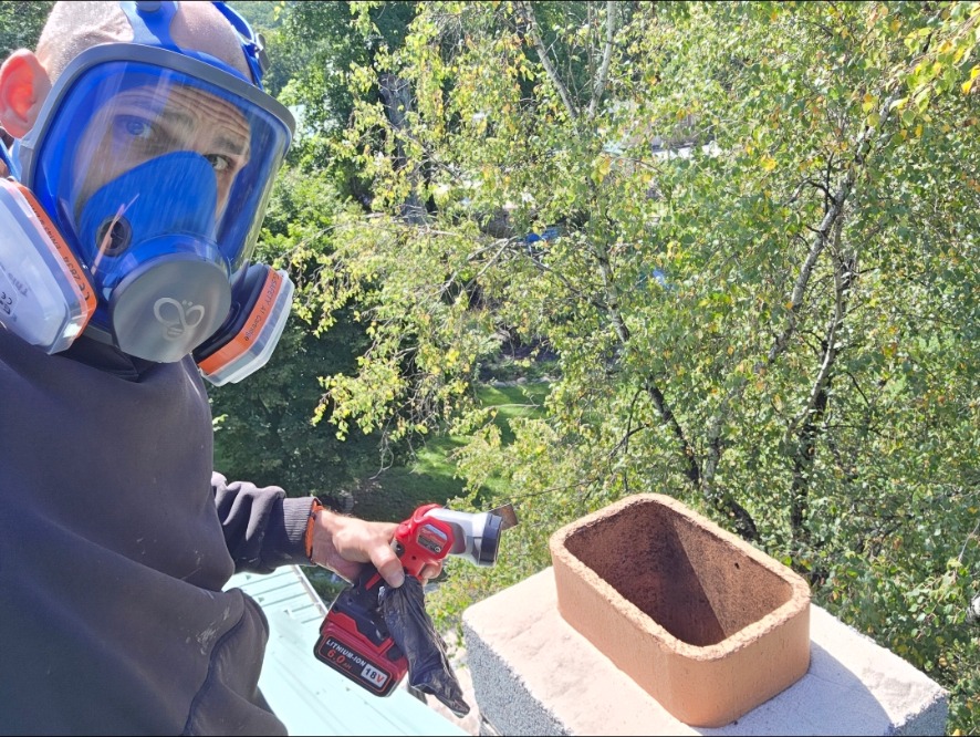 Chimney sweep wearing a respirator while working beside an open rooftop flue